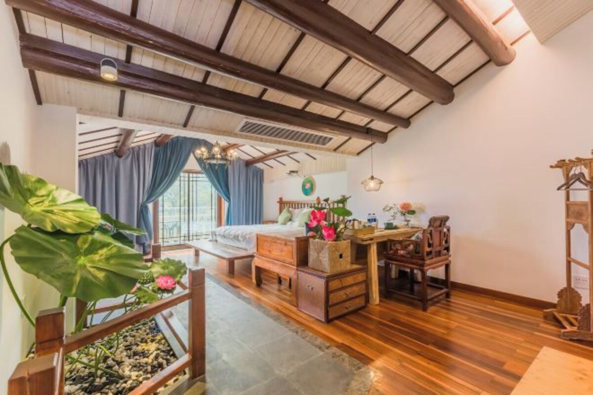 Un dormitorio con una cama de madera, un escritorio, una silla, una planta grande y vistas al exterior.