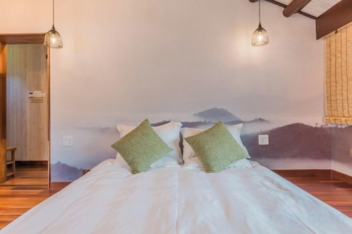 A bed with pillows, a wooden floor, a wall mural, and two hanging lights.