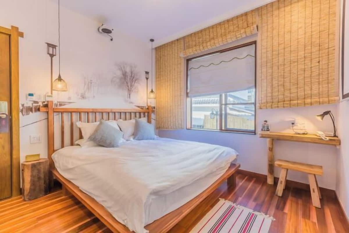 Een slaapkamer met een houten bed, een klein bureau, een raam met uitzicht en een houten vloer.