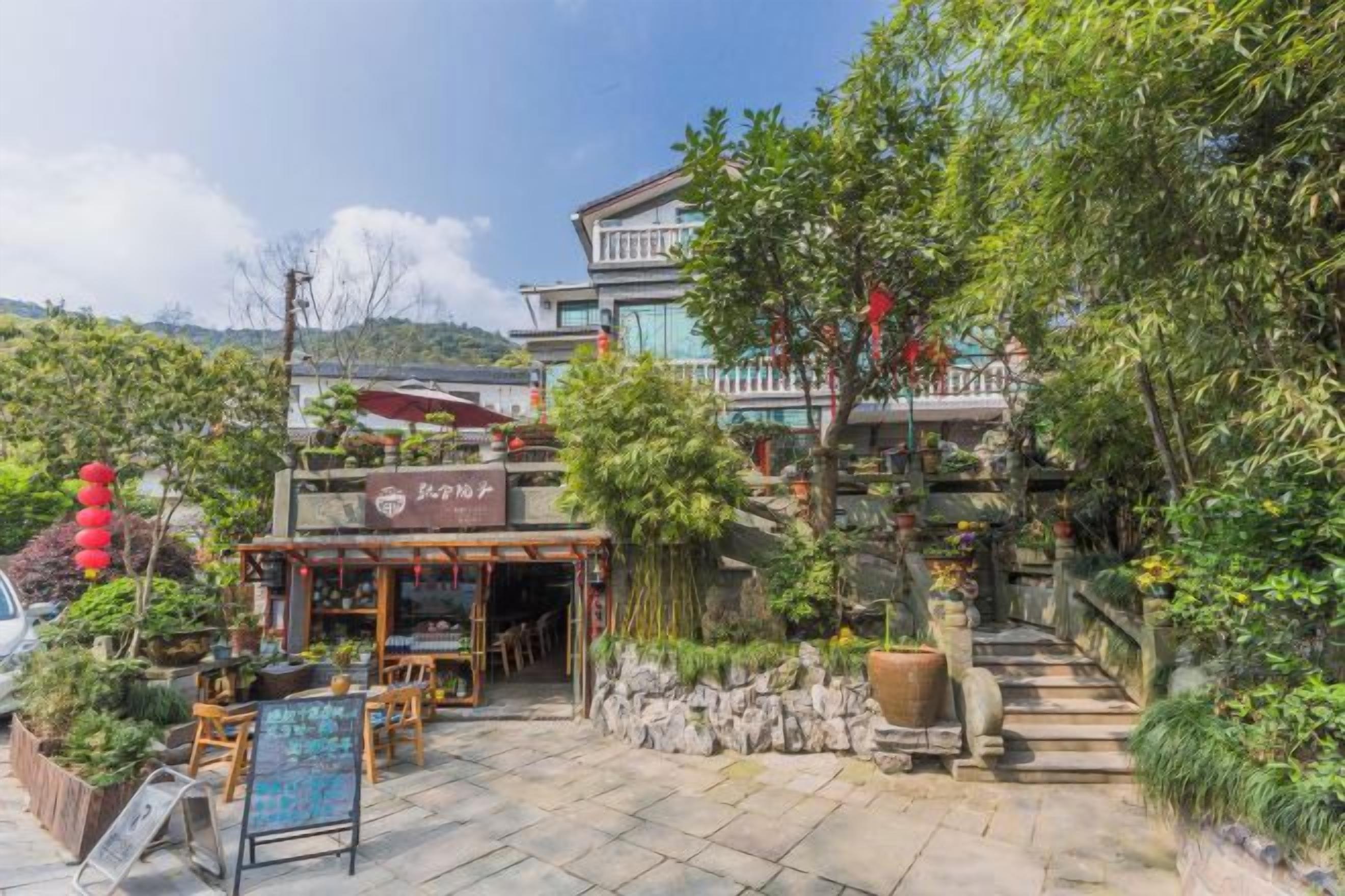 Un restaurante con terraza, rodeado de follaje y una escalera que lleva a un edificio.
