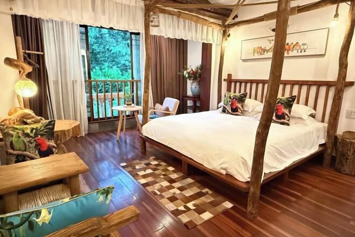 Een slaapkamer met een hemelbed, houten vloeren, een geruit tapijt, een klein tafeltje en een stoel.
