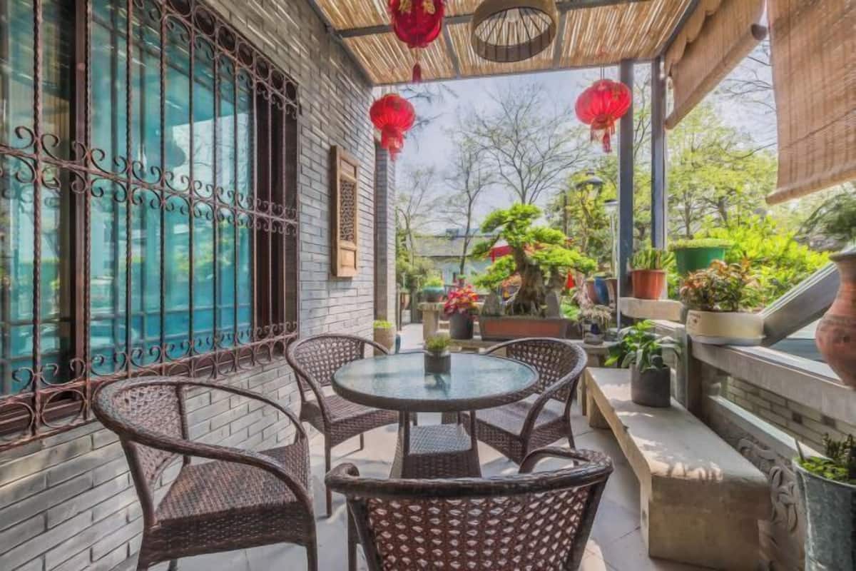 Een overdekt terras met rieten meubels, potplanten en rode lantaarns.