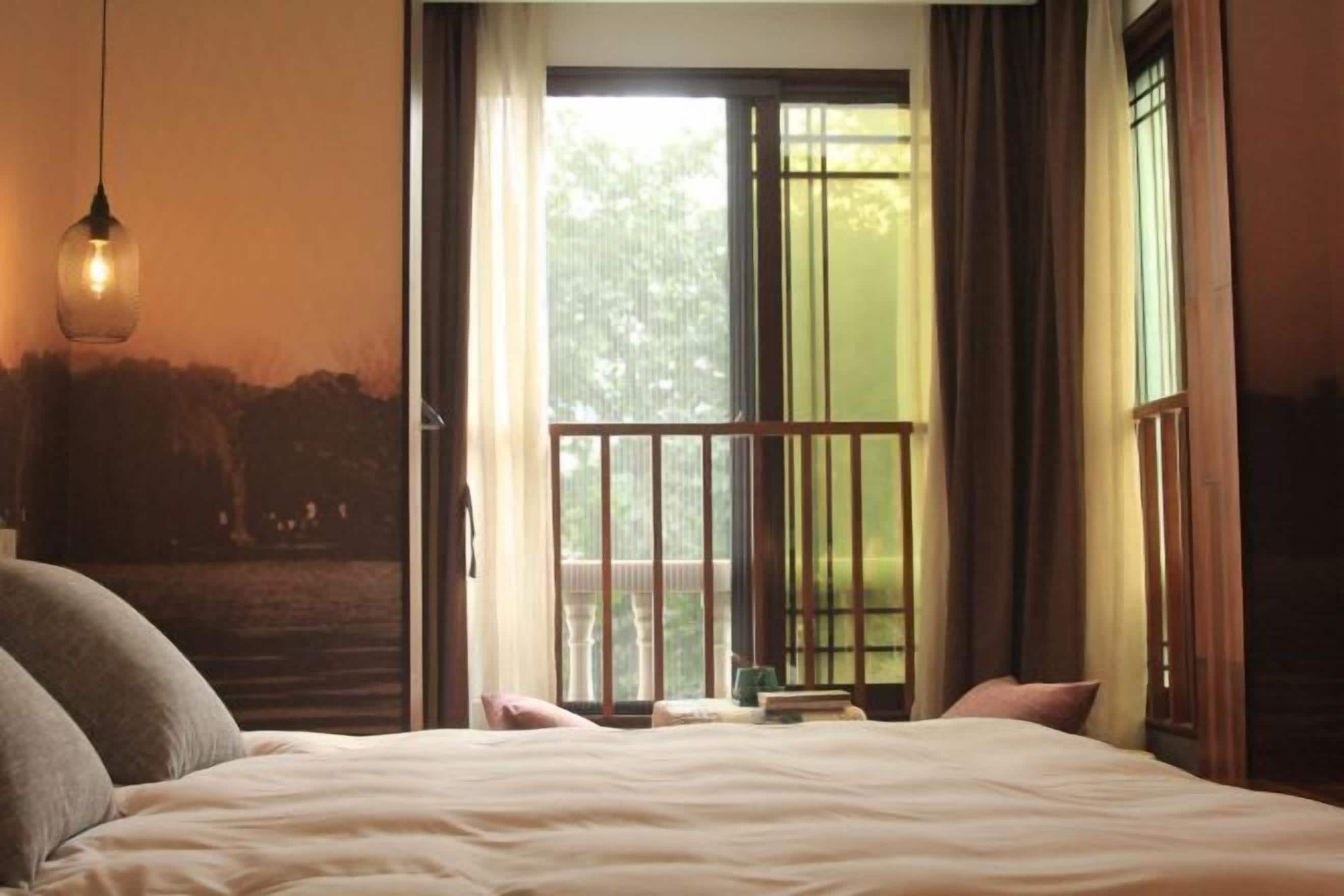 Un dormitorio con cama, una lámpara colgante, una ventana con cortinas y vistas a la vegetación exterior.