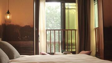 Un dormitorio con cama, una lámpara colgante, una ventana con cortinas y vistas a la vegetación exterior.
