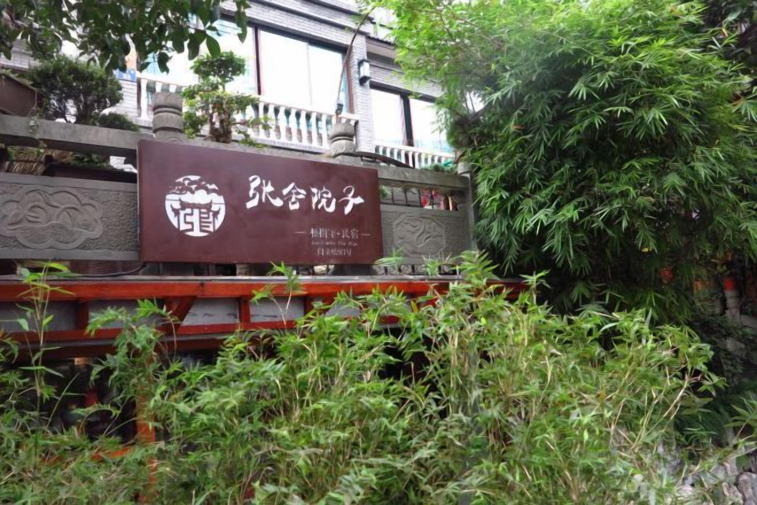 Une enseigne avec des caractères chinois, un bâtiment traditionnel et une végétation luxuriante.