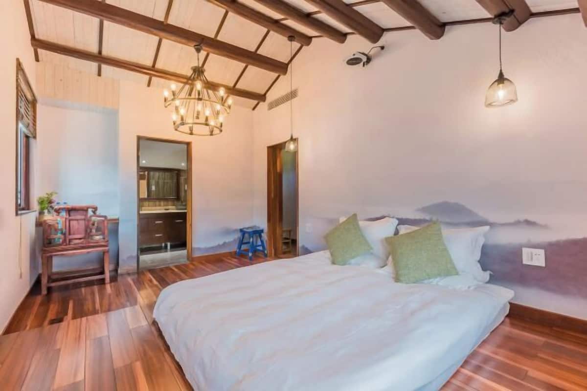 Een slaapkamer met een groot bed, houten vloeren, een kroonluchter en een bergdecoratie op de muur.