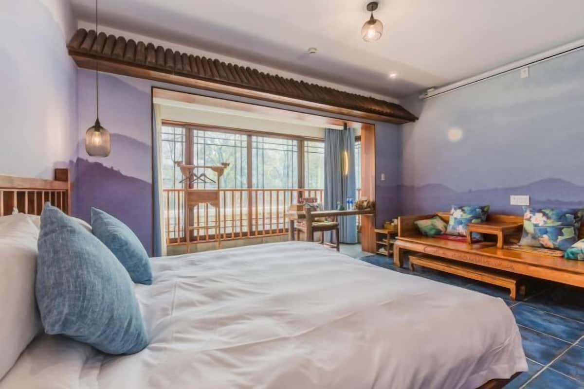 Een slaapkamer met een groot bed, een bureau en uitzicht op de omgeving door een schuifdeur.