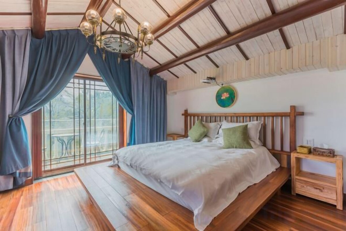A bedroom with a wooden bed, a nightstand, a wall clock, and a window with curtains.