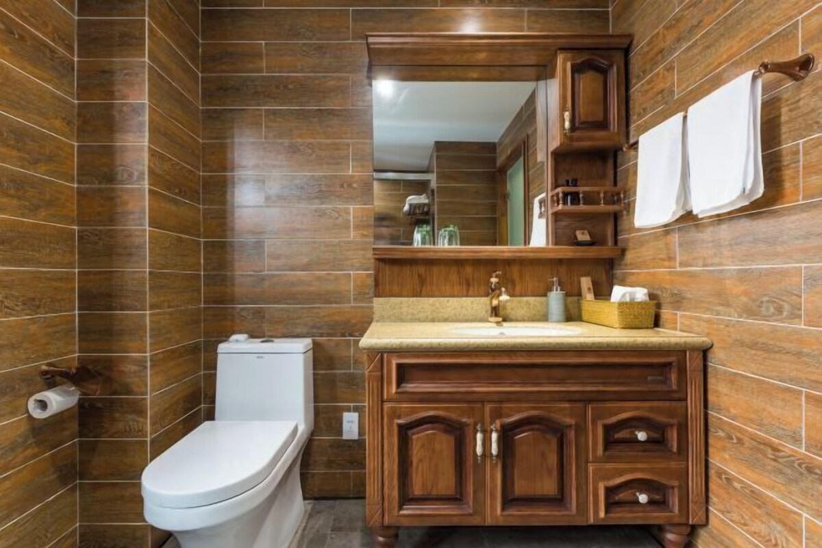 A bathroom with wooden walls, a white toilet, a wooden vanity with a mirror, and a towel rack.