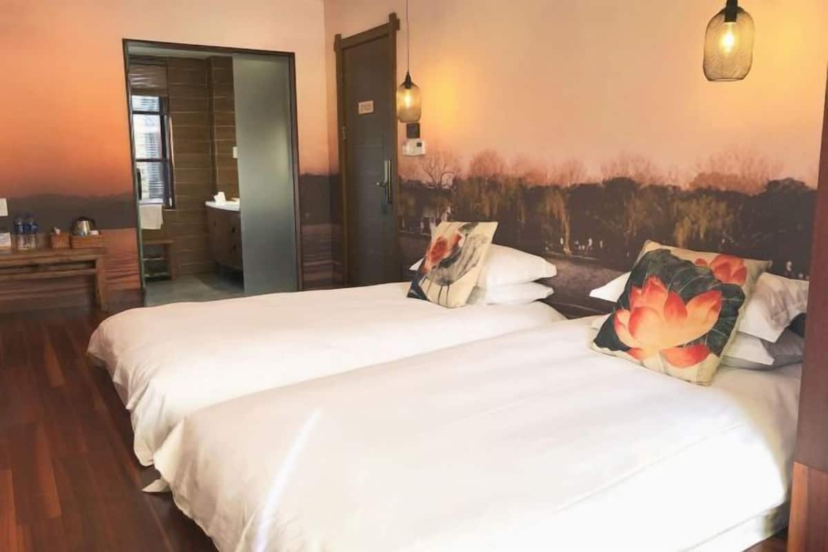 Hotelkamer met twee bedden, een houten dressoir, een badkamer die door een open deur zichtbaar is, en een muurschildering op de muur.