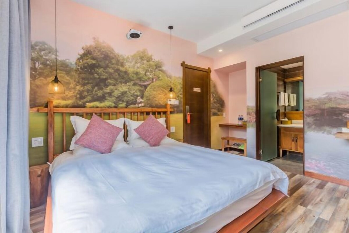 A bedroom with a bed, a wooden headboard, a door, and a wall mural.