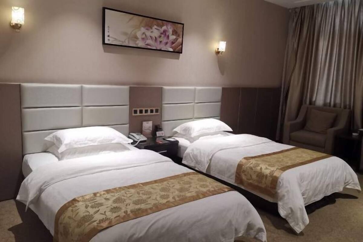 A hotel room with two beds, a nightstand, a chair, and a painting on the wall.