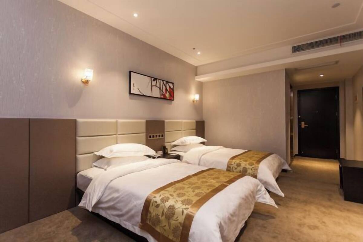 A hotel room with two beds, a headboard, wall-mounted light fixtures, and a framed artwork.