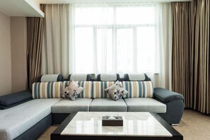 Un salon moderne avec un canapé d’angle, une table basse et des rideaux légers.