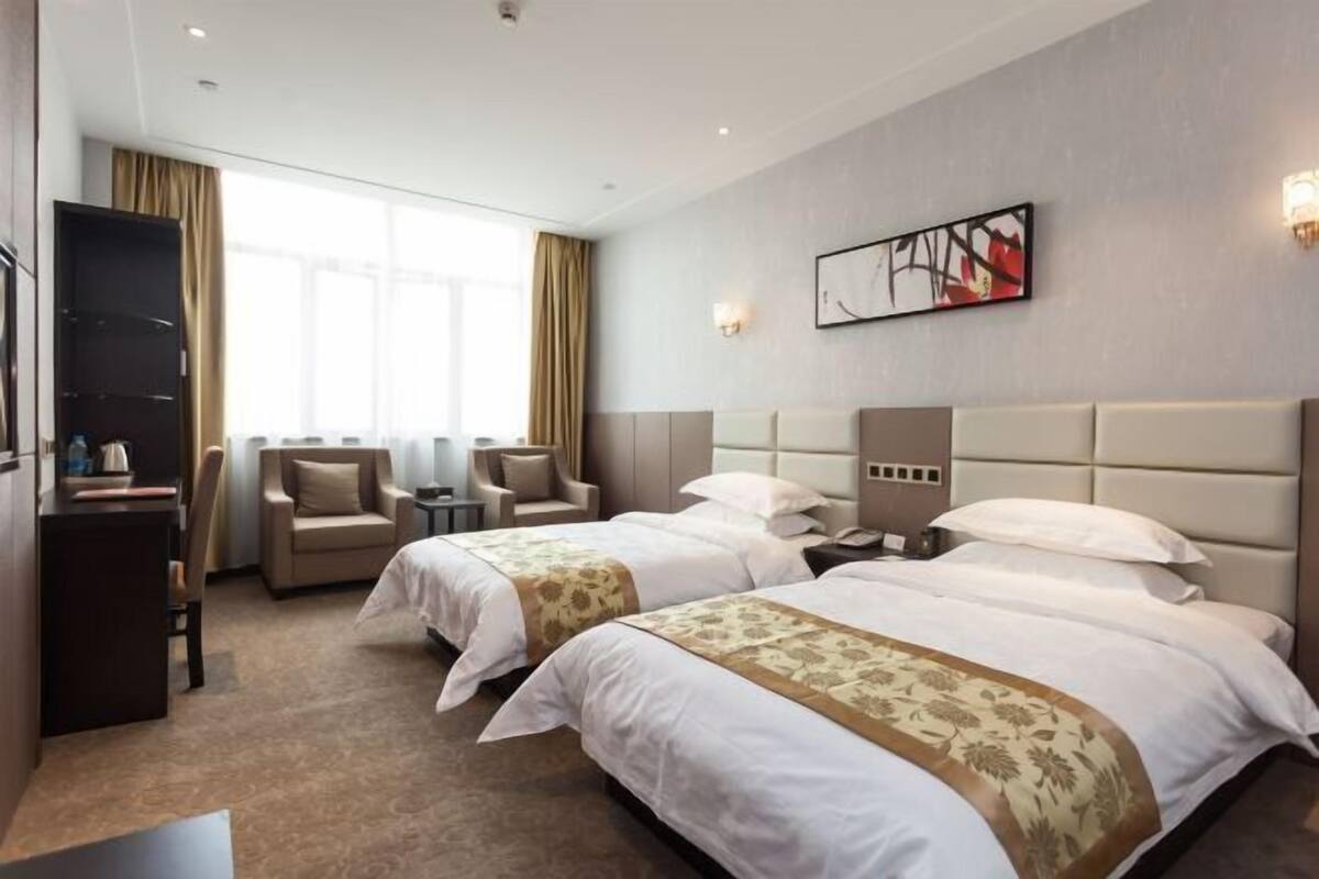 A hotel room with two beds, a desk, a chair, and a large window.