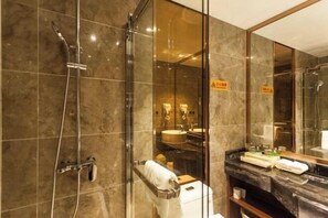 Une salle de bain moderne dotée d’une douche à parois de verre, d’un mur recouvert de carreaux de marbre, d’un grand miroir et d’un meuble-lavabo avec un évier et un porte-serviettes.