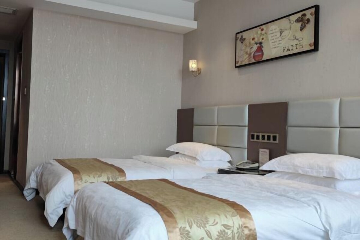 Une chambre d’hôtel avec deux lits, une tête de lit, un téléphone fixé au mur et un tableau encadré.