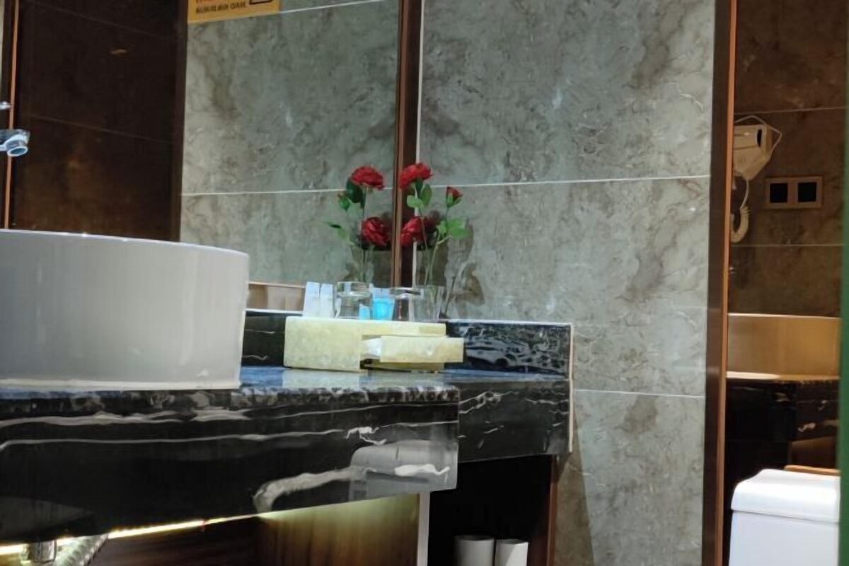 Une salle de bain avec un comptoir en marbre, un miroir et un vase rempli de fleurs rouges.
