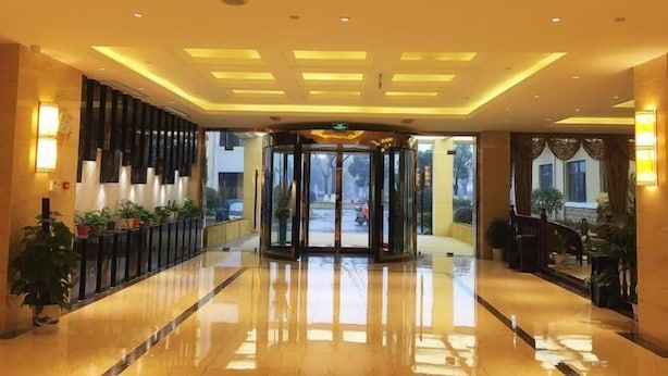Un vestíbulo de hotel con piso pulido, una puerta giratoria y plantas en macetas.