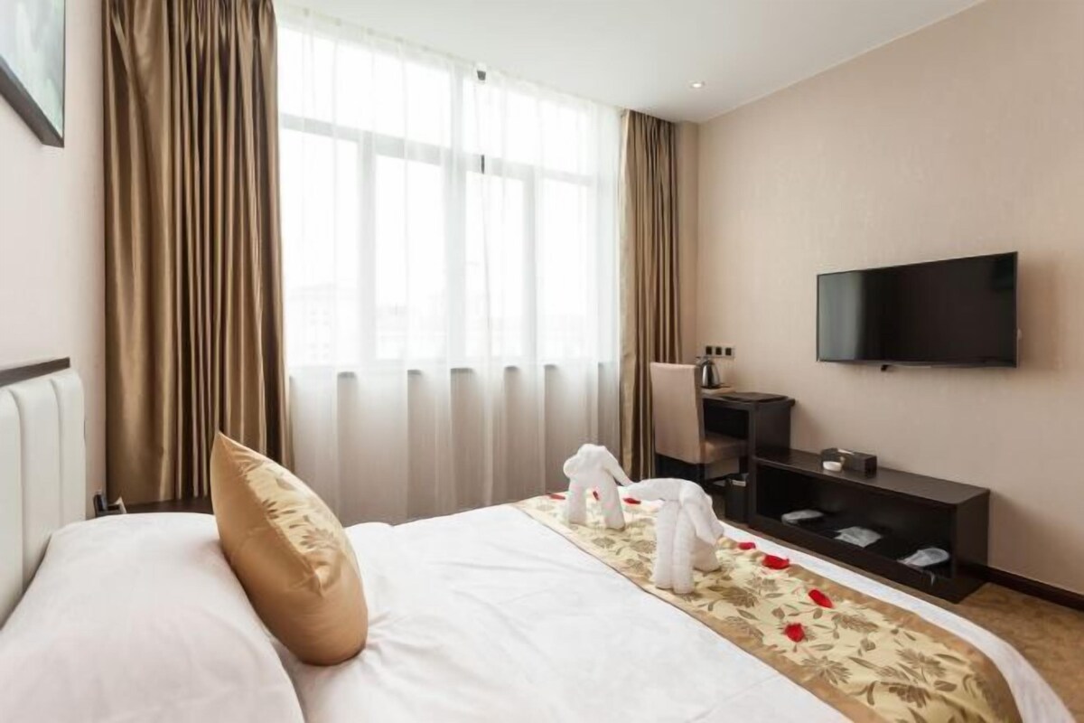 Une chambre d’hôtel avec un lit, une télévision, une table de chevet et une fenêtre avec des rideaux.