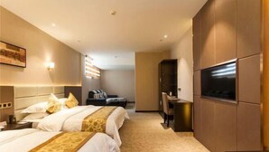 Habitación de hotel con dos camas, un escritorio, un televisor y una zona de estar con sofá y sillones.