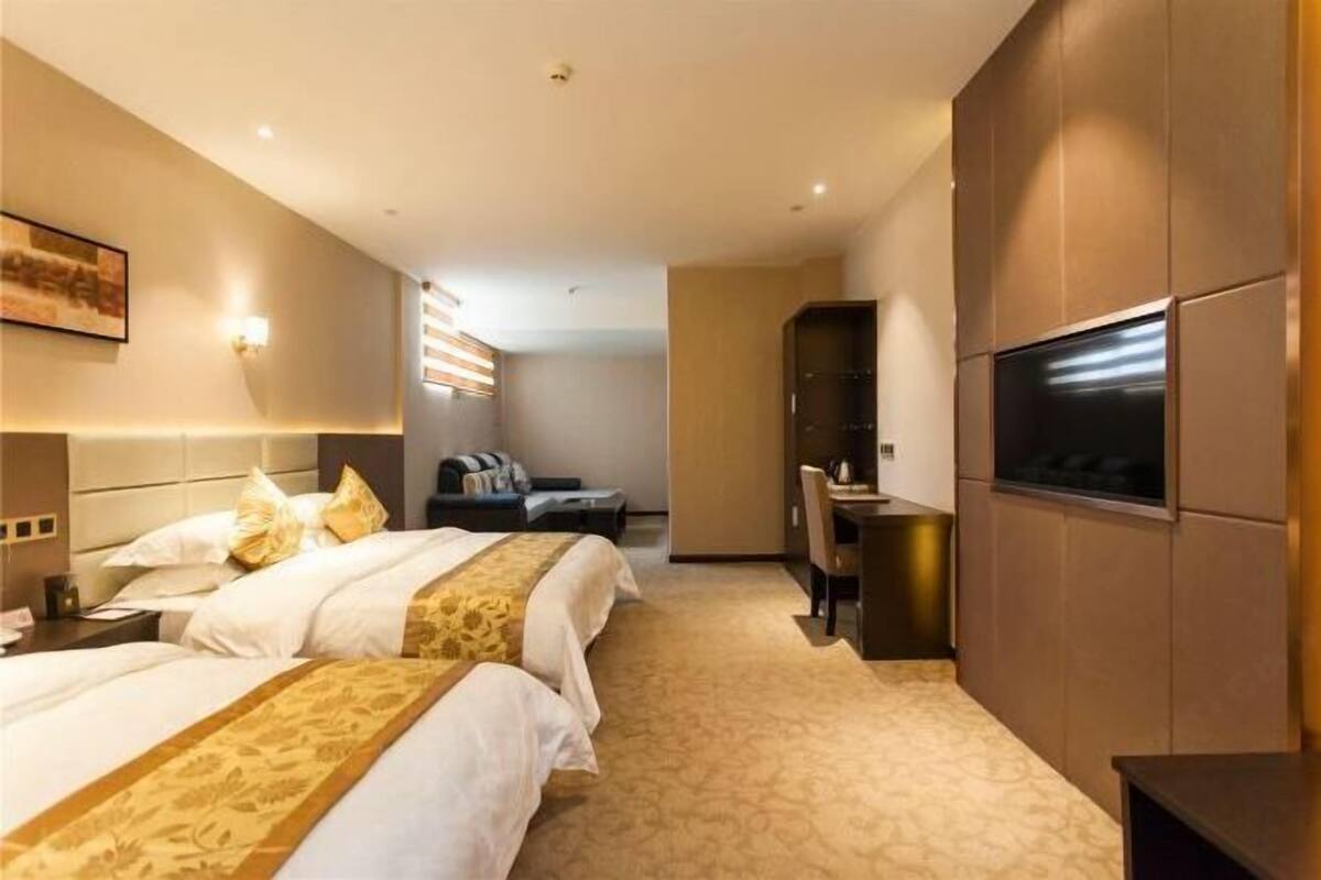 A hotel room with two beds, a desk, a TV, and a seating area with a sofa and chairs.