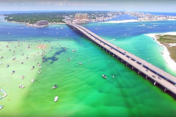 A coastal bridge with boats in the water, a beach, and a cityscape in the background.