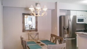 A dining area with a wooden table, chairs, a chandelier, a refrigerator, and a microwave.