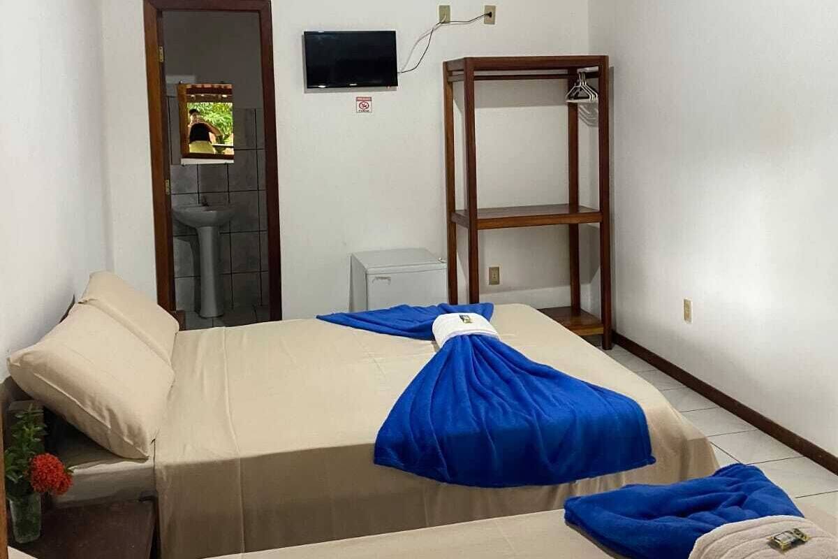 A room with a wooden ceiling, a bed with beige and blue bedding, a small table, a mirror, and a television mounted on the wall.