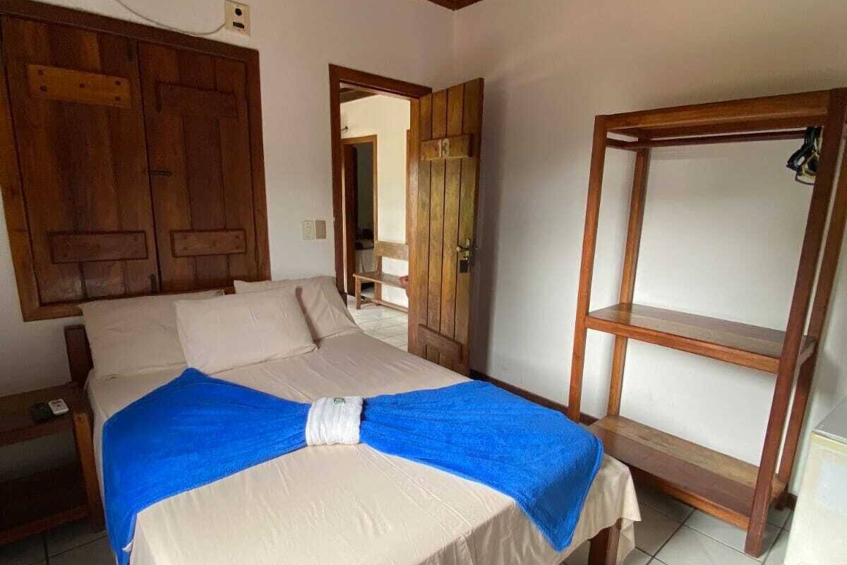 A bedroom with a bed, wooden wardrobe, and a shelf.