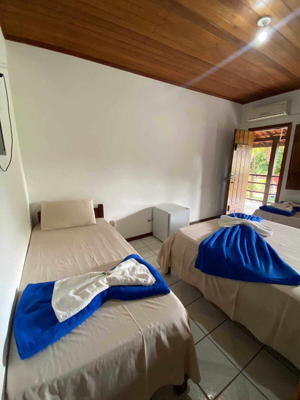 Quarto com duas camas, uma mesinha e uma janela com a porta aberta.