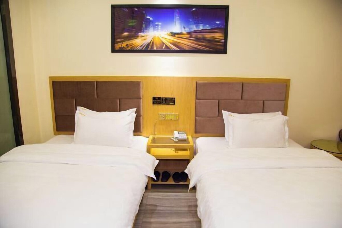 A hotel room with two beds, a nightstand with a phone, and a cityscape painting above.