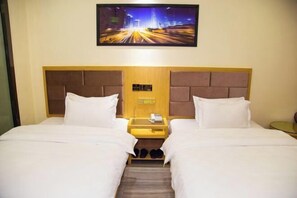 Habitación de hotel con dos camas, una mesita de noche con teléfono y un cuadro de un paisaje urbano.