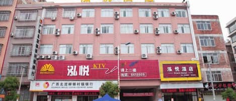 A multi-story hotel with a red facade, multiple air conditioning units, and several ground-level shops.