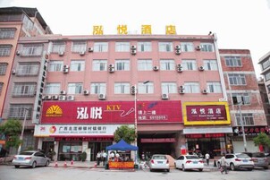 Un hotel de varios pisos con fachada roja, múltiples unidades de aire acondicionado y varias tiendas a nivel de calle.