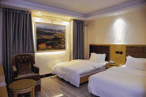 Habitación de hotel con dos camas, una silla, una mesita, un cuadro en la pared y una ventana con cortinas.
