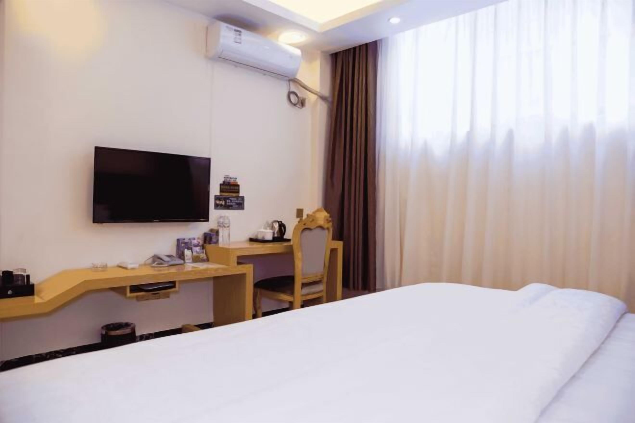 Habitación de hotel con cama, escritorio con silla, televisión y ventana con cortinas.
