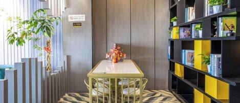 A room with a patterned floor, a table with chairs, a bookshelf with books and plants, and a vertical garden.
