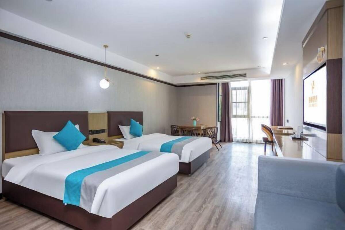 A hotel room with two beds, a desk, a chair, and a large window.
