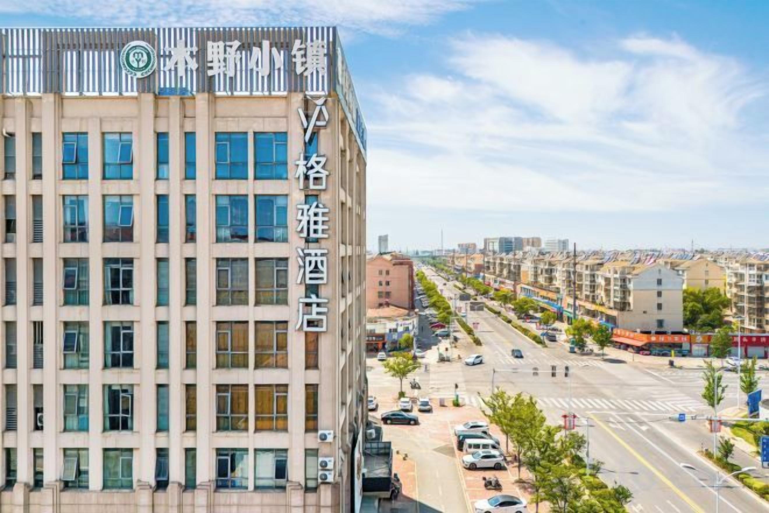 Un hotel de varios pisos con fachada moderna, situado en una calle concurrida y tráfico visible, con coches estacionados.