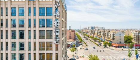 Un hotel de varios pisos con fachada moderna, situado en una calle concurrida y tráfico visible, con coches estacionados.