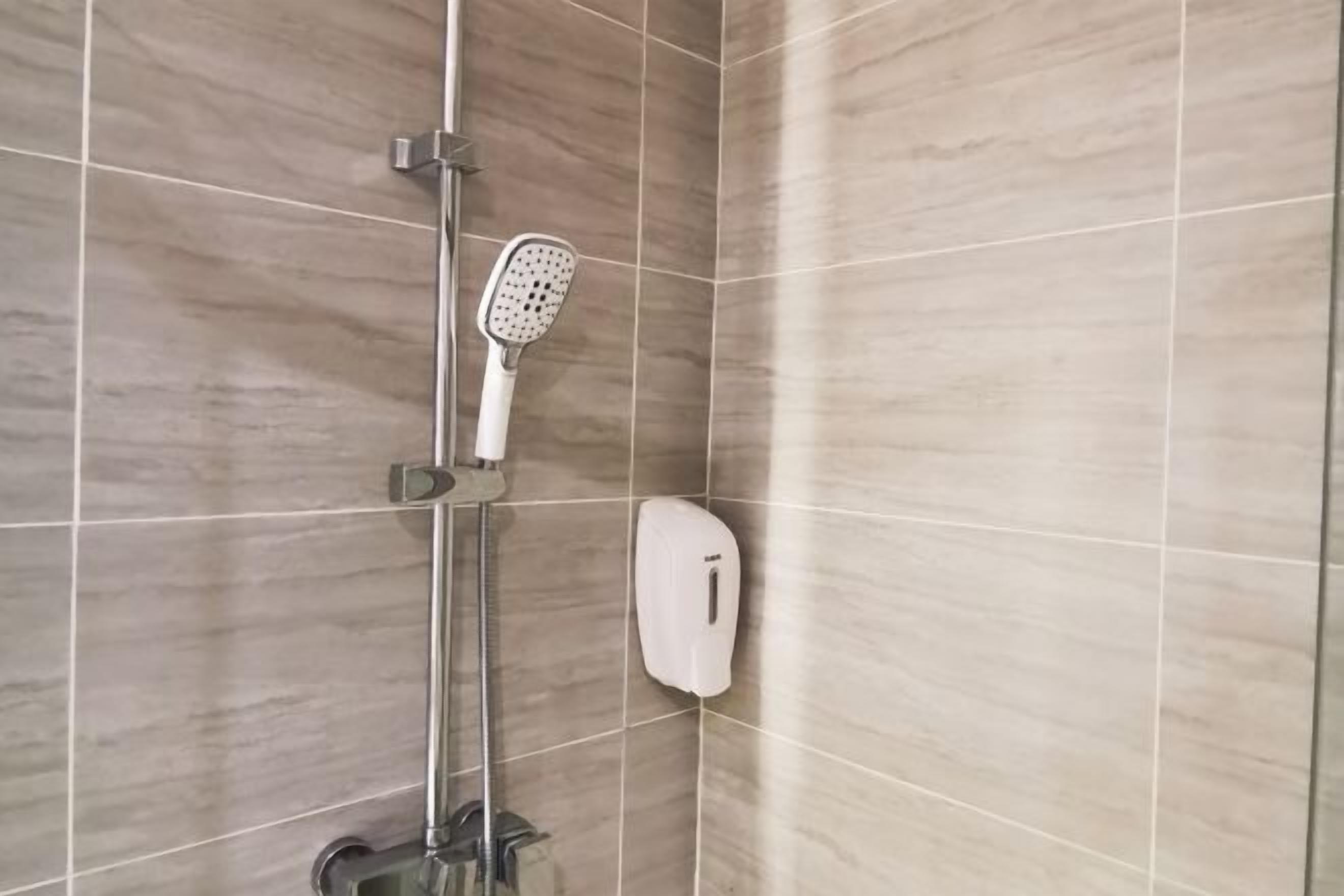 A shower area with a handheld showerhead and a soap dispenser on the wall.