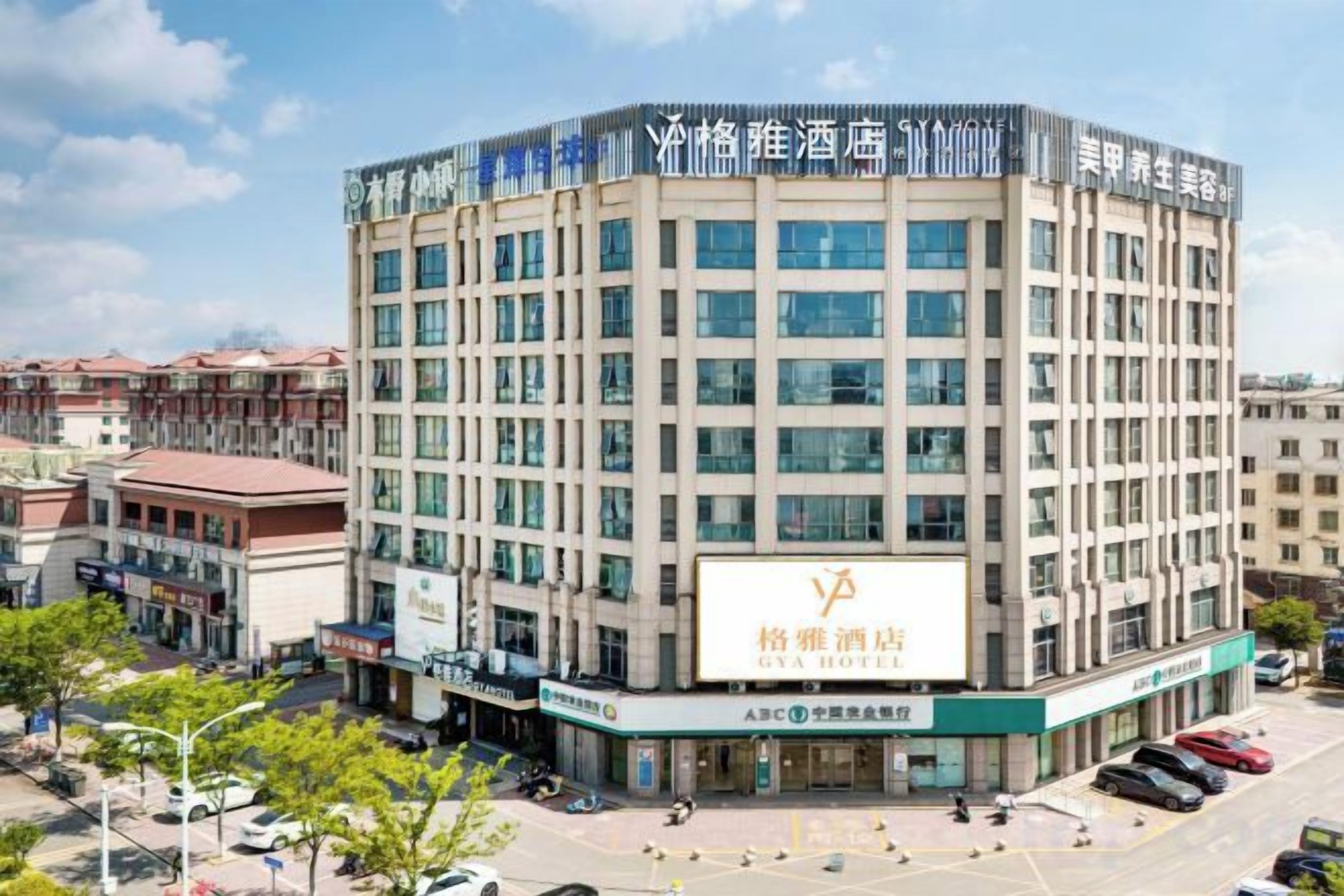 Hotel de vários andares com entrada central, cercado por um estacionamento e outros edifícios.