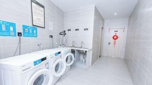 A modern laundry facility with two front-loading washing machines, a sink, and a mirror. - GYA Hotell(Jingjiang gongsuoqiao store&Jiangyin Industrial Park ) (Jingjiang)