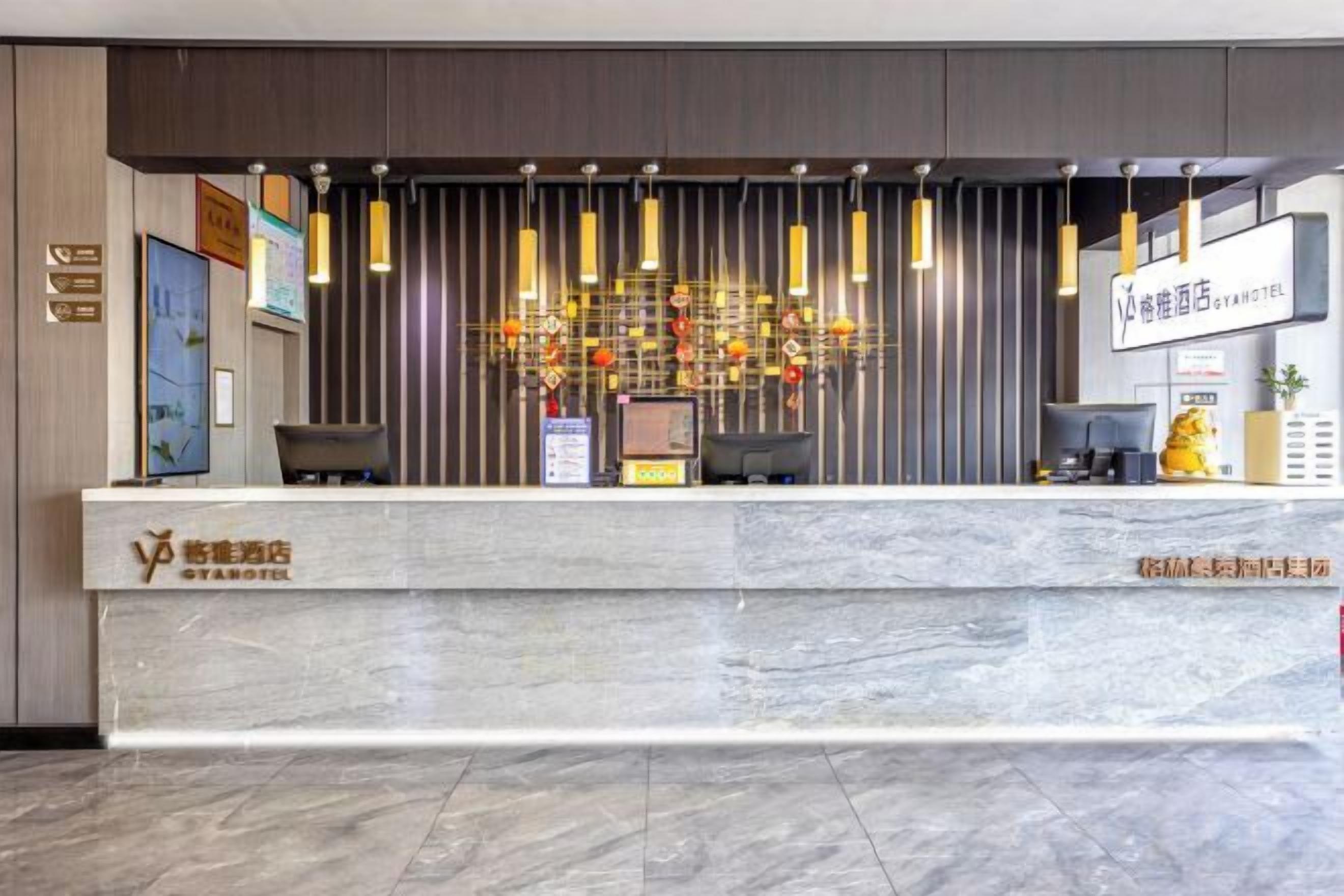 A hotel reception desk with a marble counter, a modern chandelier, and a sign indicating the hotel name.