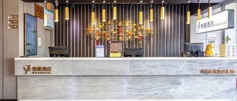 A hotel reception desk with a marble counter, a modern chandelier, and a sign indicating the hotel name.