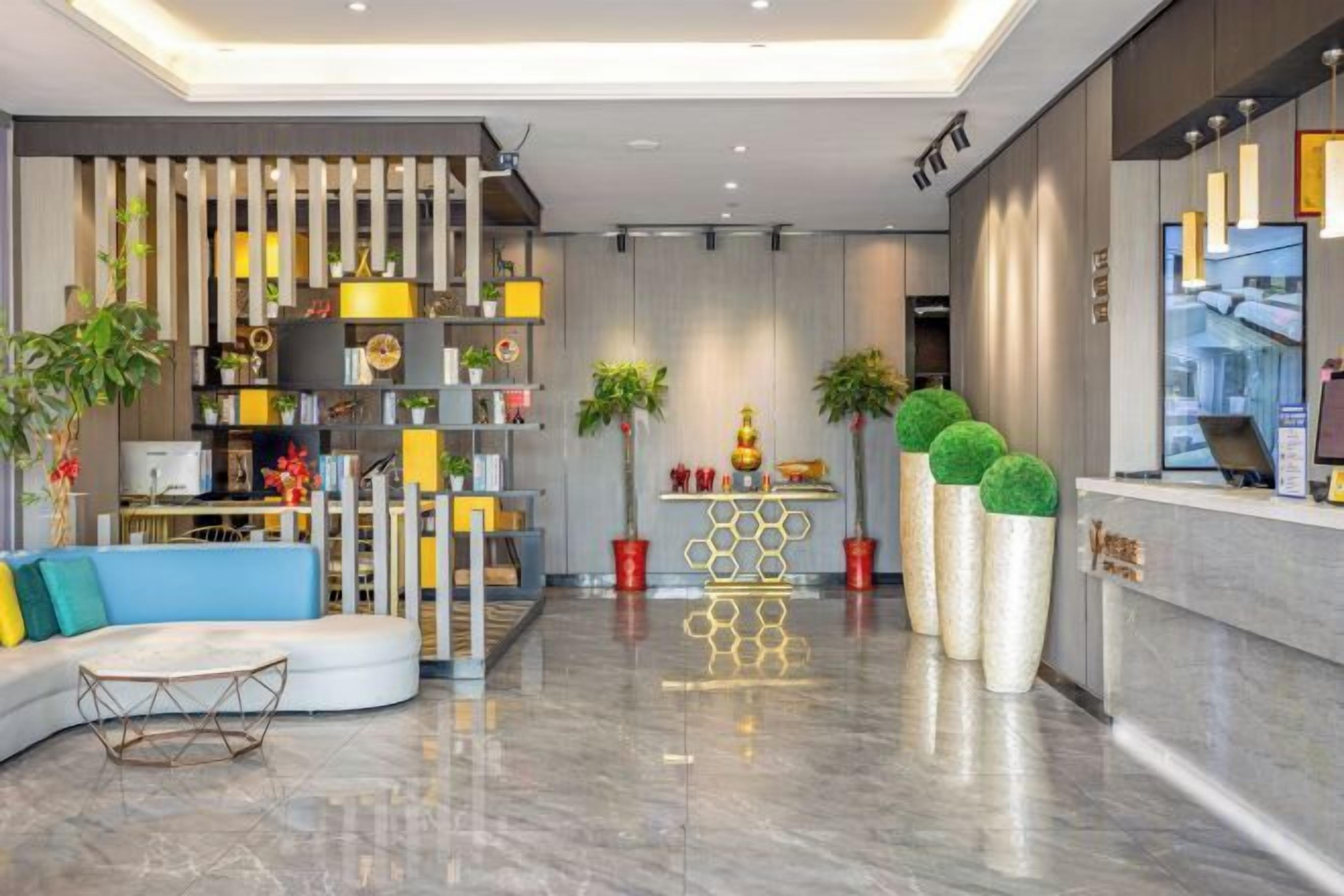 A modern hotel lobby with a reception desk, seating area, and decorative plants.