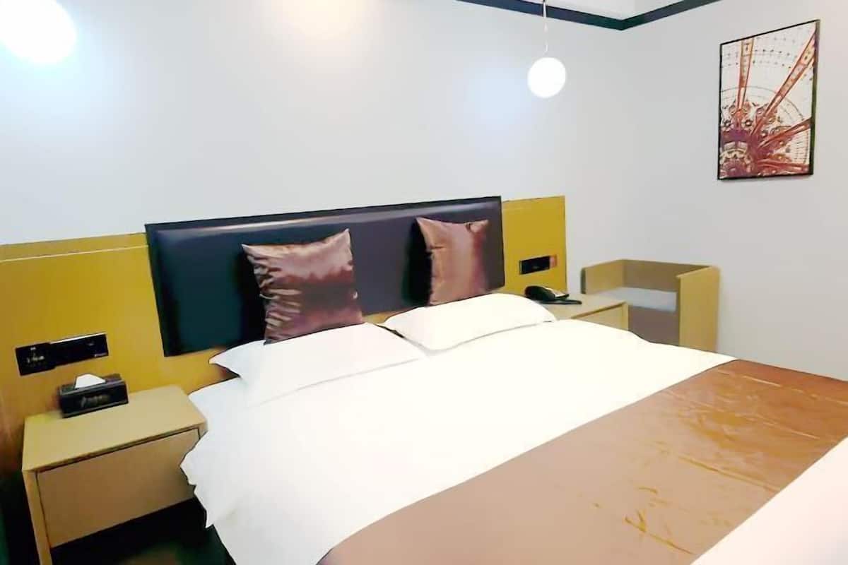 A hotel room with a bed, bedside tables, a nightstand, a wall-mounted light, and a picture.