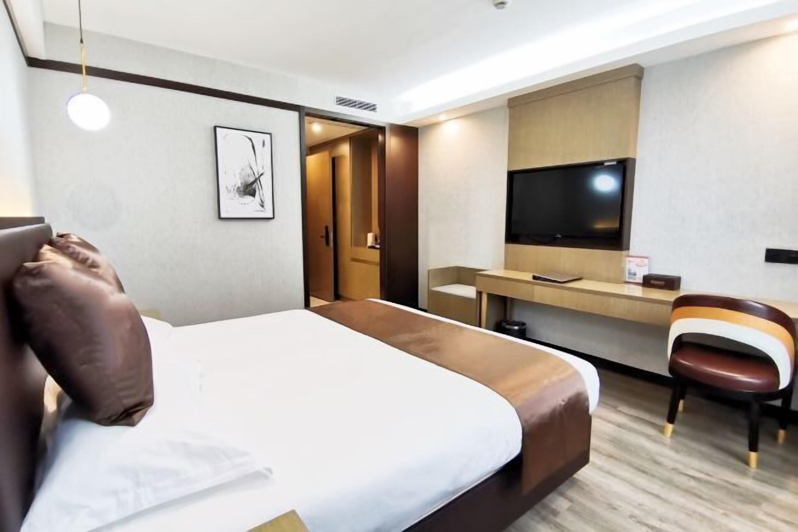 Une chambre d’hôtel avec un lit, un bureau, une chaise, une télévision et un tableau encadré au mur.