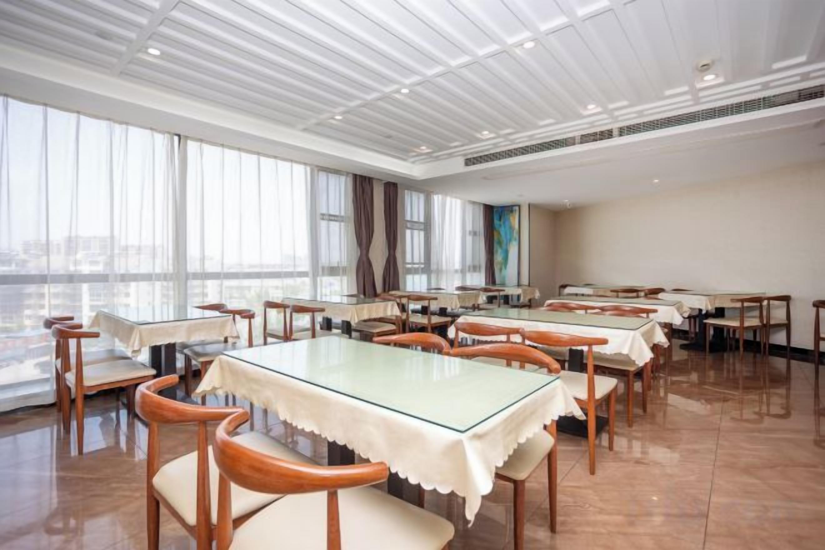 A spacious dining area with multiple tables and chairs, large windows, and a high ceiling.